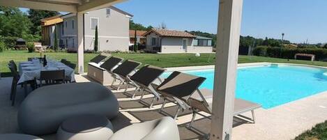 A covered outdoor area with a pool, lounge chairs, and a table with chairs.