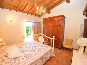A bedroom with a bed, wooden wardrobe, chair, and a chandelier. - La Capannella Del Cinema by Interhome (Capannori)