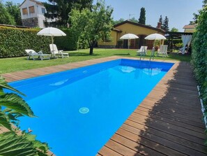 A rectangular swimming pool with a wooden deck surrounding it, a grassy area with trees, and a building in the background. - La Capannella Del Cinema by Interhome (Capannori)