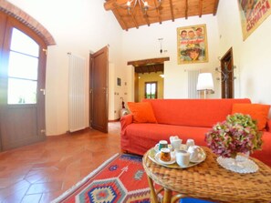 A room with a red sofa, a wicker table with a tray of items, a patterned rug, and a door leading to another room. - La Capannella Del Cinema by Interhome (Capannori)