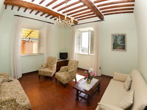 Una sala de estar con un sofá, dos sillones, una mesa de centro de madera, un televisor y un cuadro en la pared.