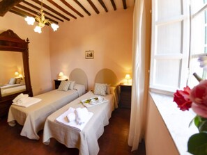 Une chambre avec deux lits simples, un grand miroir, une table de chevet avec une lampe et une fenêtre donnant sur un beau paysage.