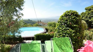 A swimming pool surrounded by greenery, two green chairs, and a view of distant hills. - Alla Collina Del Sole by Interhome (Ciciana)