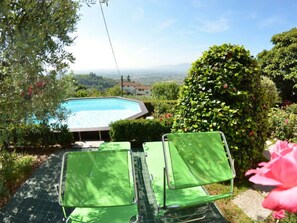 Ein Pool, umgeben von Grünflächen, zwei grüne Stühle und eine Aussicht auf ferne Hügel.