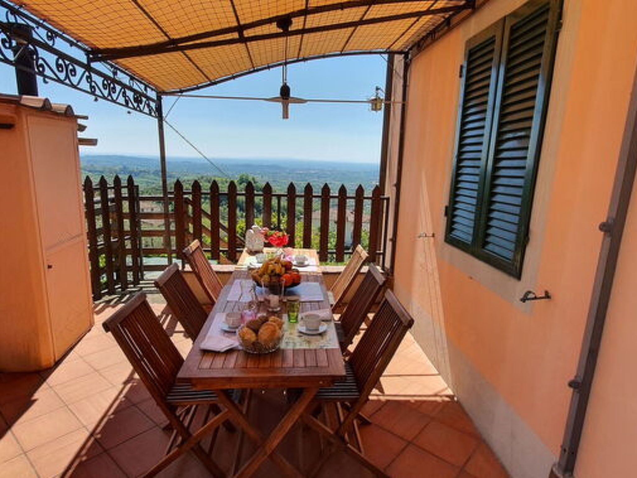 Un área de comedor al aire libre techada, con una mesa para dos, vista al mar y una cerca de madera.