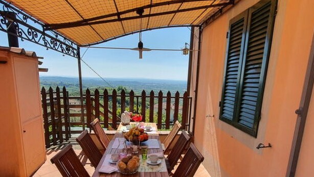 A covered outdoor dining area with a table set for two, a view of the sea, and a wooden fence. - Alla Collina Del Sole by Interhome (Ciciana)