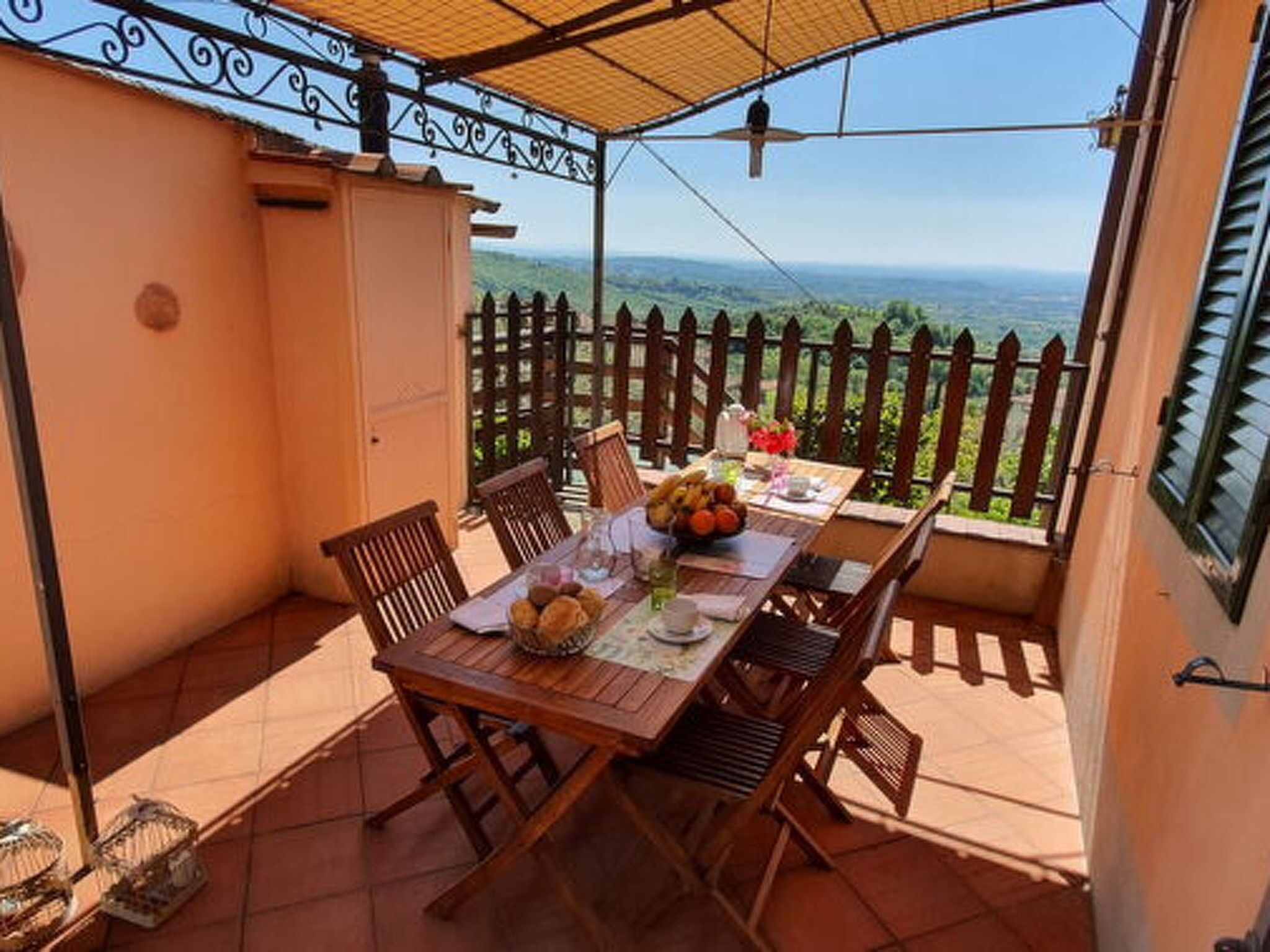 Een houten tafel met stoelen op een balkon, met uitzicht op het landschap en een hek.