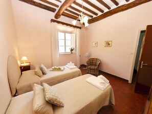 Una habitación con dos camas, una silla, un ventanal y una puerta.