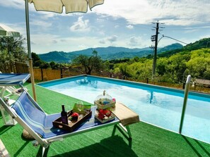 Ein Swimmingpool mit Blick auf Berge, eine Liege und ein Tisch mit einer Flasche und einem Buch.