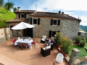 Una casa de pedra amb un pati que disposa d'una taula preparada per dinar, seients a l'aire lliure i plantes en testos.