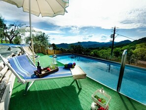 Ein Pool mit Liegestühlen, ein Tisch mit Getränken und Blick auf Berge.