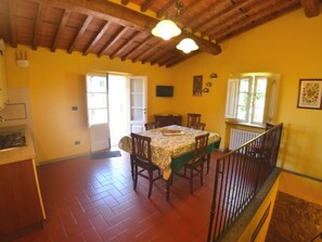 A dining area with a table set for four, wooden chairs, a ceiling with exposed beams, and a window with a view of greenery outside. - Podere Aida Proprietà by Interhome (Capannori)