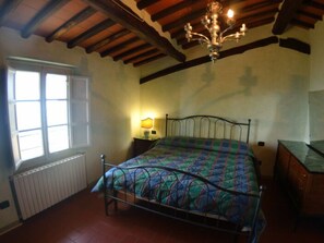 Une chambre à coucher avec un lit, un radiateur, une fenêtre, une table de chevet et un lustre.