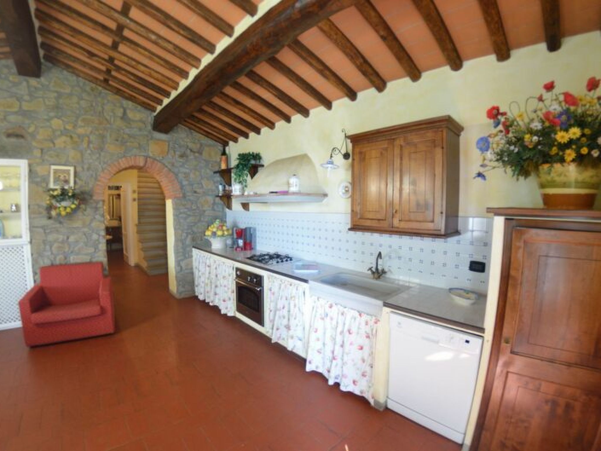 A kitchen with stone walls, wooden beams, a red chair, and a white countertop.