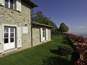 Un bâtiment en pierre avec des volets blancs, une pelouse bien entretenue et une vue sur le paysage.