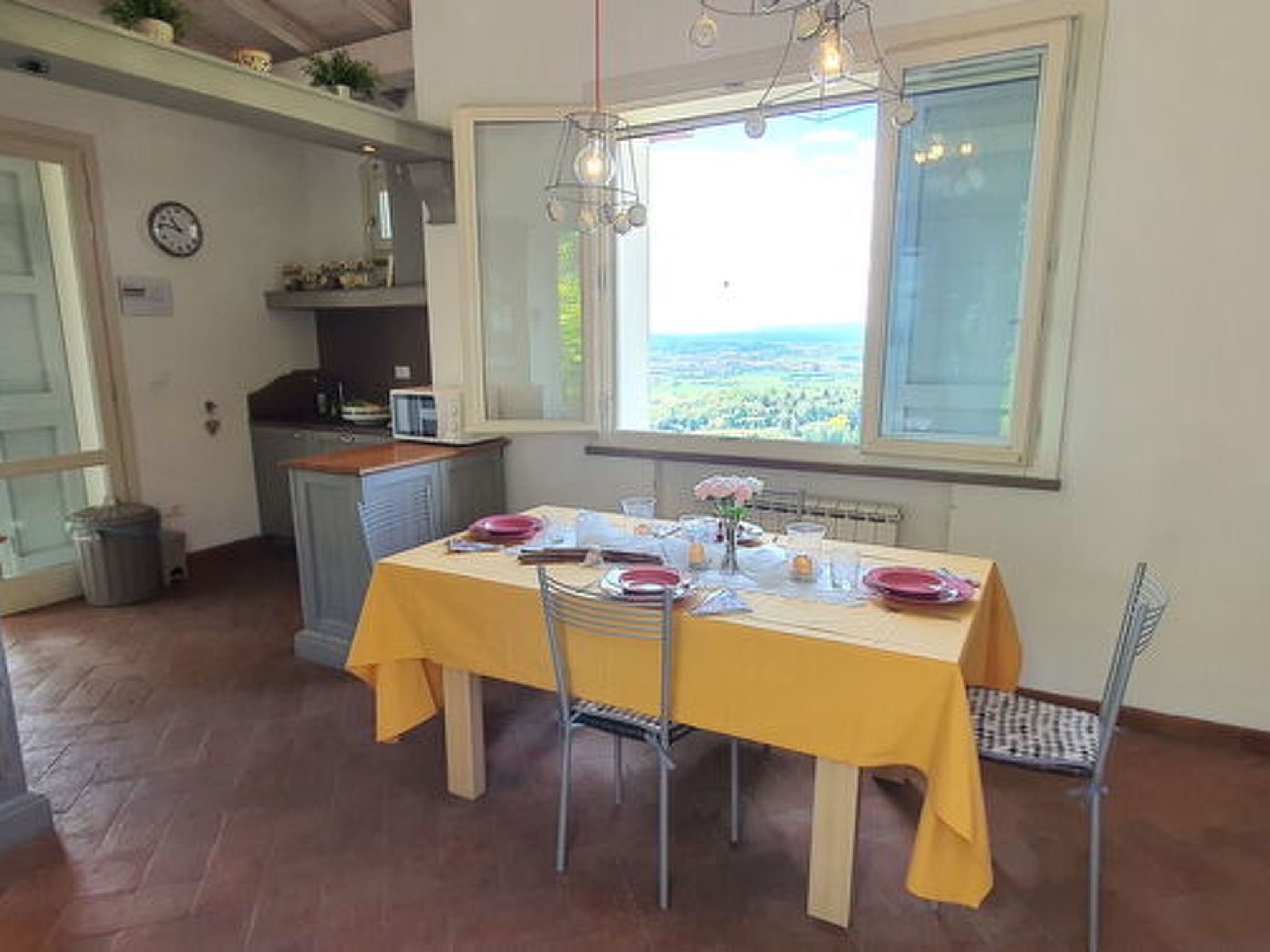 A dining area with a table set for four, a window with a view, and a kitchen in the background.