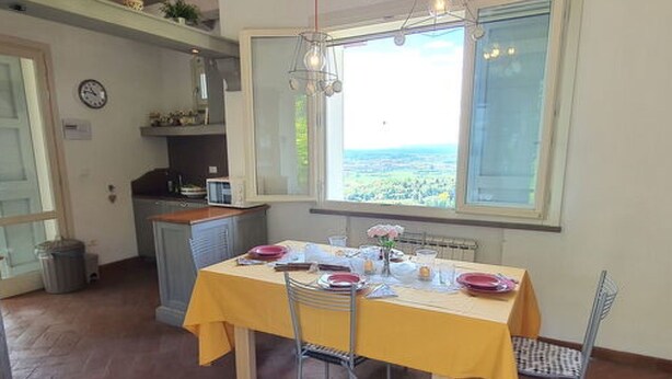 Un comedor con una mesa dispuesta para cuatro, una ventana con vistas y una cocina al fondo.