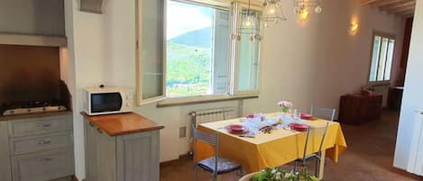 A kitchen with a dining table set for two, a bowl of fruit on the counter, and a view of the outdoors through a window.