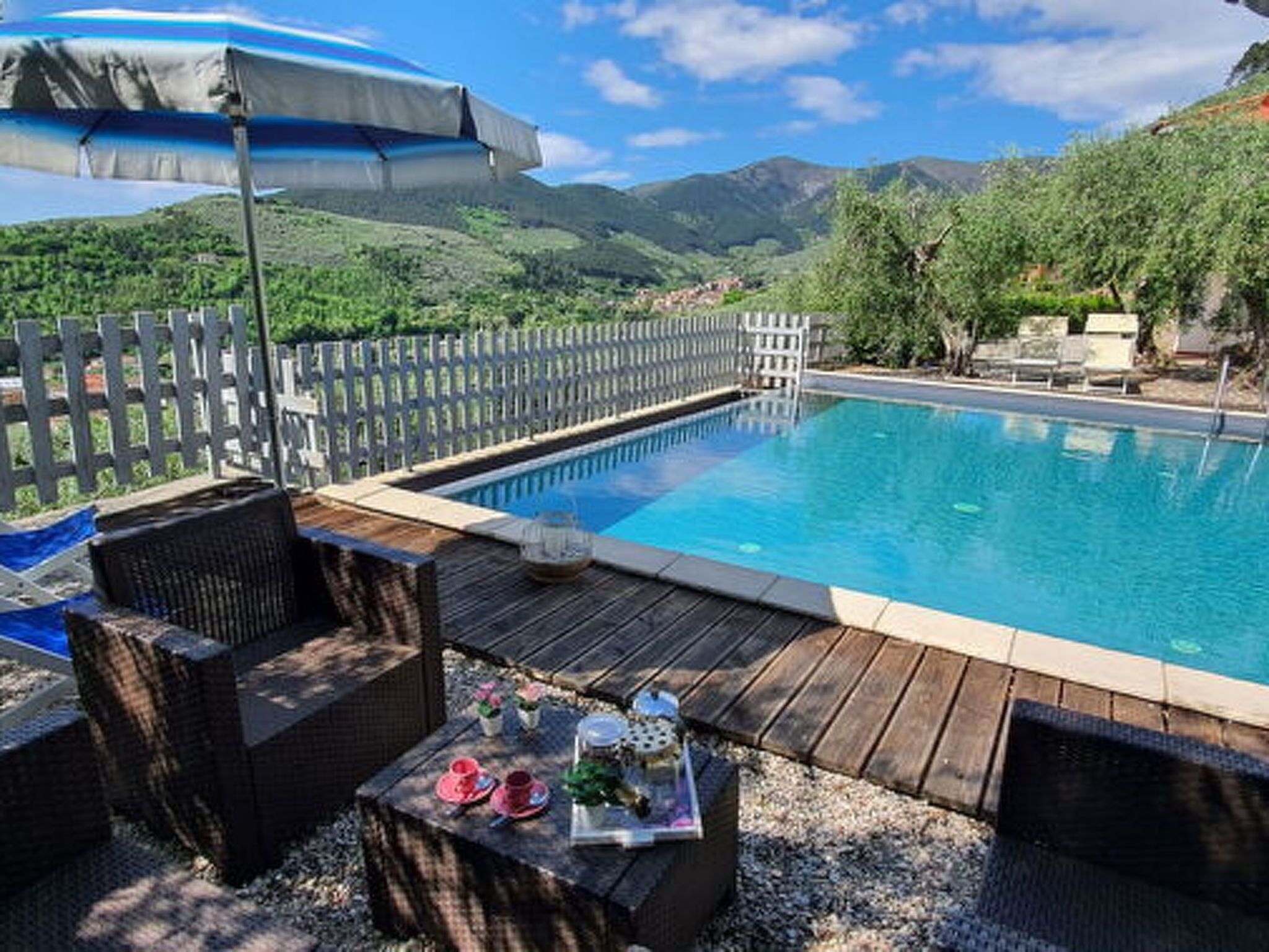 A swimming pool with a wooden deck, wicker furniture, and a view of mountains.