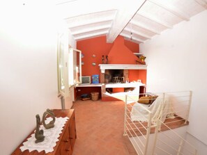 Habitació estreta amb sostre inclinat, taula petita amb objectes decoratius, estructura de llit metàl·lica blanca i paret vermella.