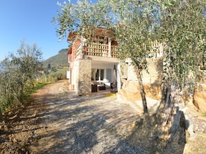 Ein Steinhaus mit Balkon, Kiesweg und Olivenbäumen.