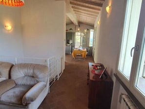 A room with a sofa, a dining table with yellow tablecloth, and a window with a view. - Podere San Martino by Interhome (Buti)