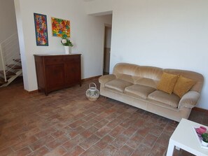 A living room with a beige sofa, a wooden cabinet, and two colorful paintings on the wall. - Podere San Martino by Interhome (Buti)
