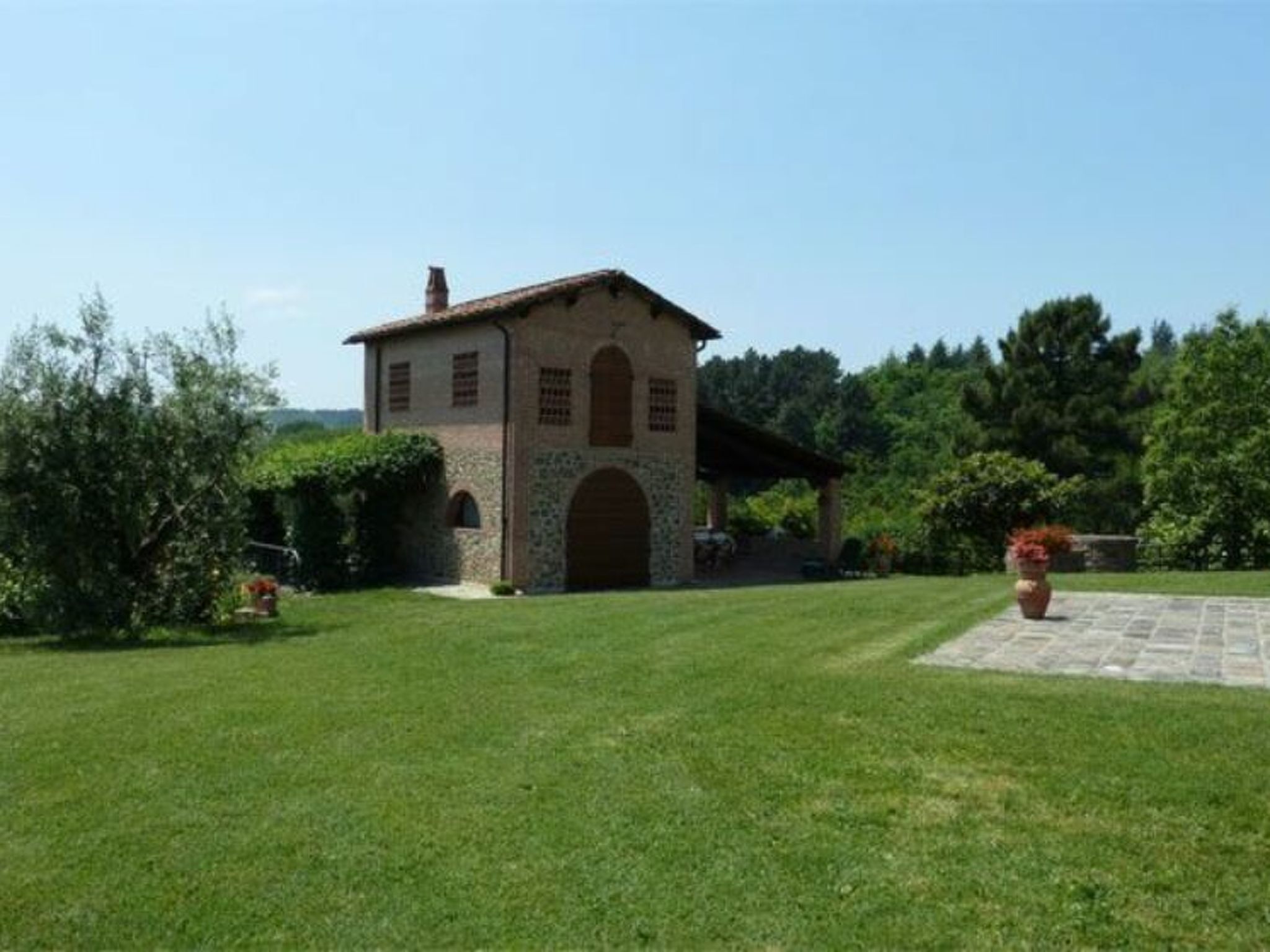 Un edificio in pietra con tetto in tegole, circondato da un prato e alberi.