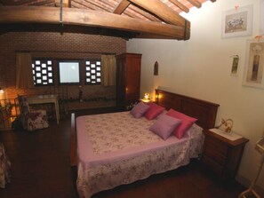 Une chambre avec un grand lit, une tête de lit en bois, une cheminée et un mur en briques.