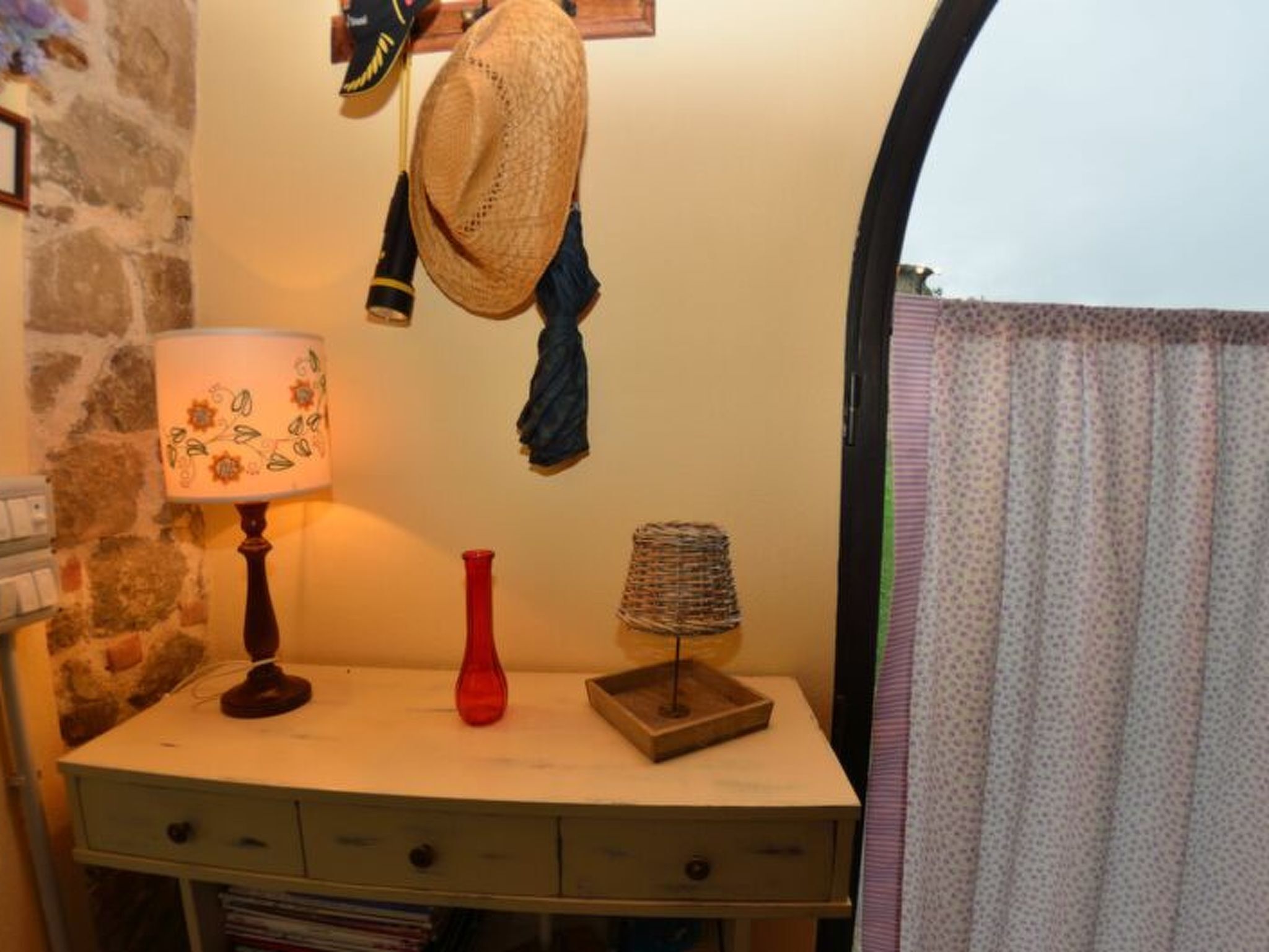 Une pièce comprenant un bureau, une lampe, un vase rouge, un panier tressé et un chapeau accroché au mur.