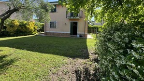 Ein zweigeschossiges Gebäude mit Eingangstür, einem kleinen Balkon und einem gepflegten Rasen.