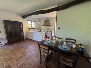 A dining area with a table set for four, a kitchen in the background, and a large wooden cabinet. - Dependance Egle by Interhome (Ciciana)