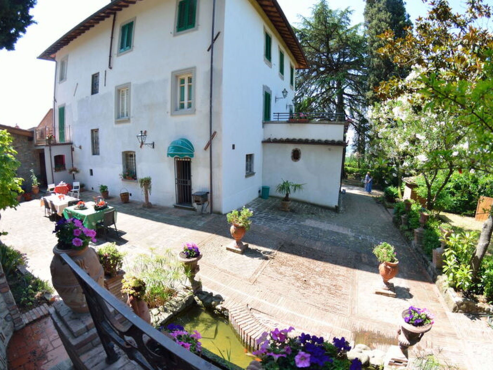 Un edificio bianco con persiane verdi, un cortile con un piccolo stagno e piante in vaso.