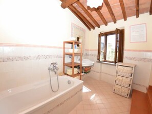 A bathroom with a bathtub, a wooden shelf, a window, and tiled walls. - Al Vecchio Pozzo by Interhome (Buti)