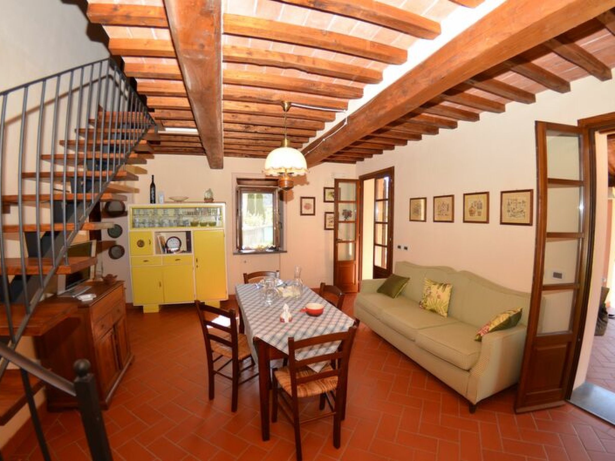 A dining area with a table and chairs, a sofa, a staircase, and a yellow cabinet.