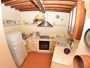 Eine kleine Küche mit Gaskochfeld, einem Kühlschrank und einer Holzbalkendecke.