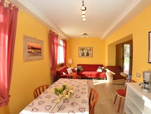 Ein Zimmer mit Esstisch, Stühlen, einer Couch, einer Kaffeemaschine und einem Bild an der Wand.