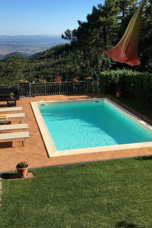 Ein rechteckiger Swimmingpool mit klarem, blauem Wasser, umgeben von einer Holzterrasse, einer Rasenfläche und einem Metallzaun.