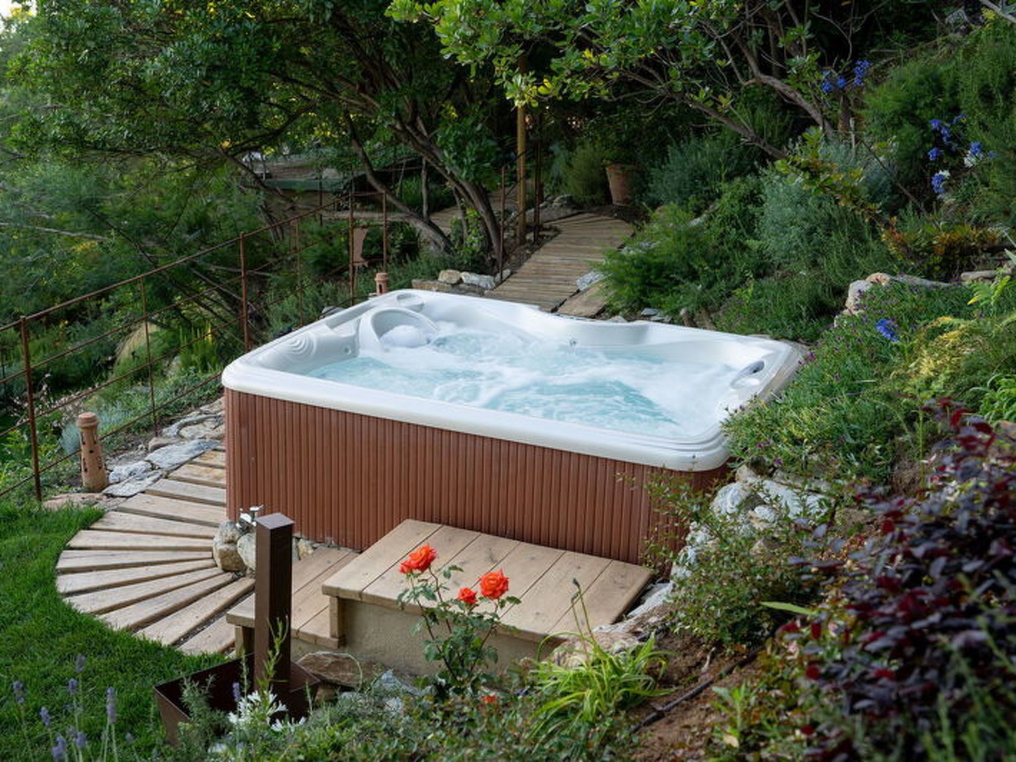 Un bain à remous entouré d’une végétation luxuriante et doté d’une terrasse en bois.