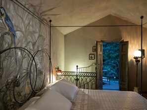 Ein Schlafzimmer mit einem Bett, einem Nachttisch, einer Wandlampe, einer Treppe und Blick ins Freie.