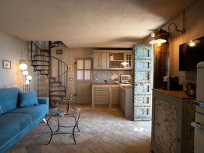Ein kompakter Wohnbereich mit Sofa, Couchtisch, Wendeltreppe, Küchenzeile und Wand-Fernseher.