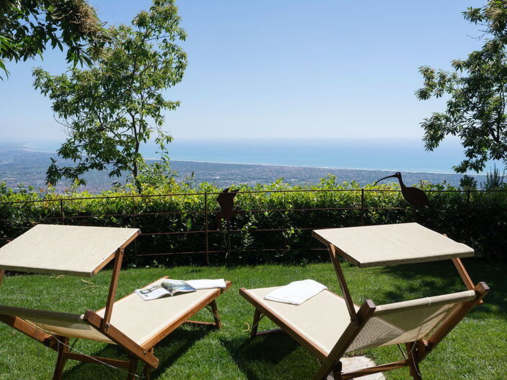 Two wooden lounge chairs with canvas seats and backs, positioned on a grassy lawn with a view of the ocean and a distant cityscape.