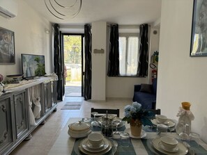 A dining area with a table set for four, a television on a cabinet, and a view through an open door. - Il Volo Del Nibbio by Interhome (Vecchiano)