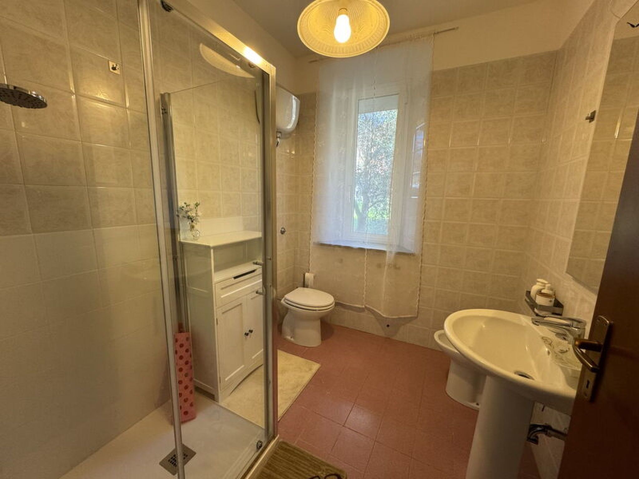 Ein Badezimmer mit Glasdusche, Toilette, Waschbecken und Fenster.