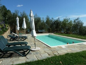 Ein Pool mit Liegestühlen und Sonnenschirmen, umgeben von viel Grün.