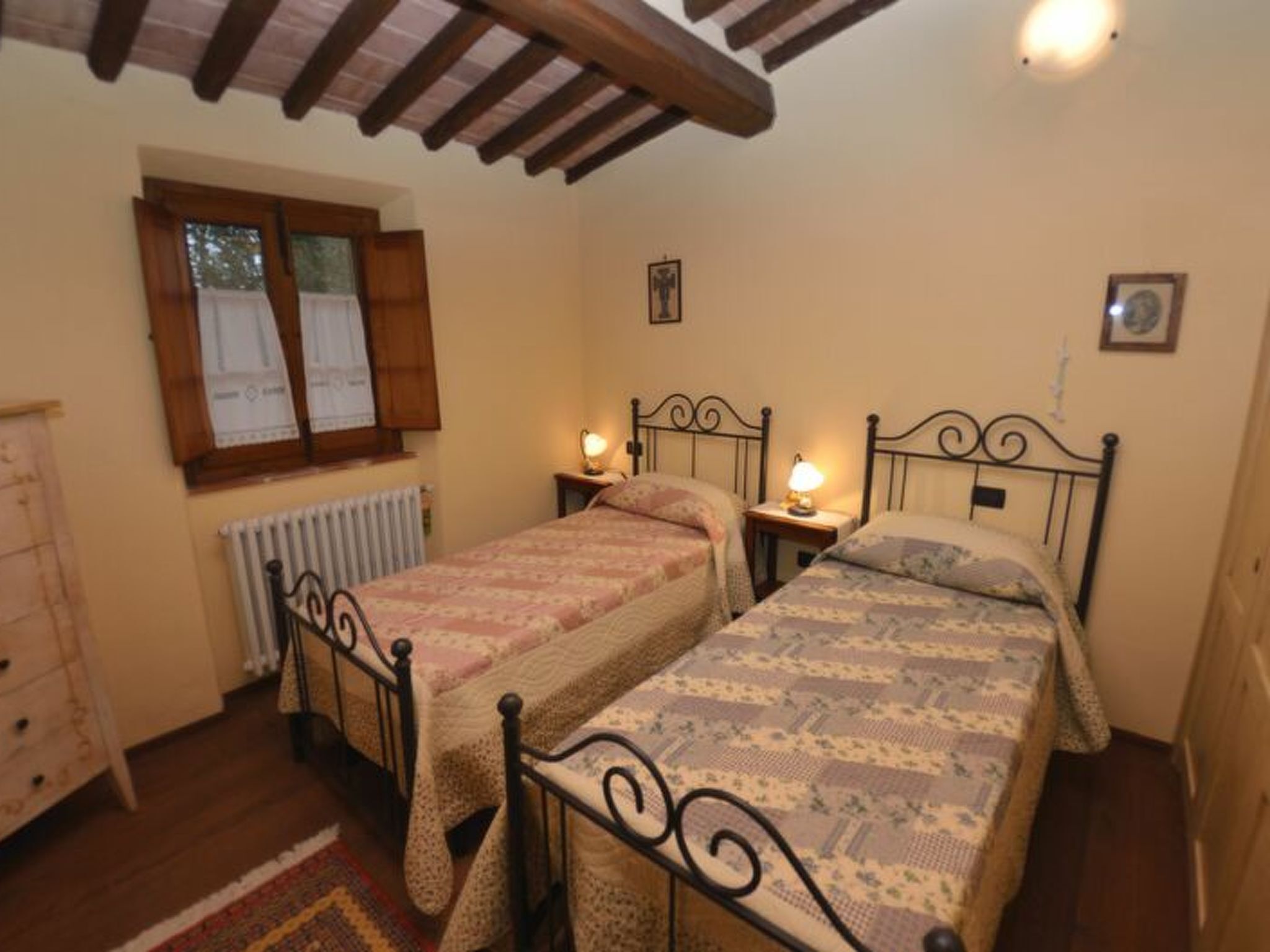 Una camera da letto con due letti, una cassettiera in legno, una finestra con persiane e un termosifone.