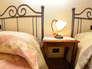 Ein Bett mit einer floralen Stegdecke, ein Nachttisch mit einer Lampe und ein Kopfteil.