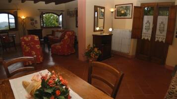 Un coin repas avec une table dressée pour deux personnes, un arrangement floral en guise de décoration centrale et une vue sur le salon.