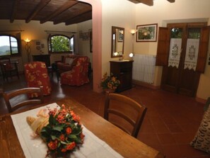 Ein Essbereich mit einem Tisch für zwei Personen, einer floralen Tischdekoration und Blick auf das Wohnzimmer.