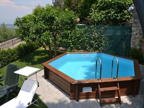 A rectangular hot tub with two ladders, surrounded by a wooden deck, with a grassy area and trees in the background. - Casa Max by Interhome (Capannori)